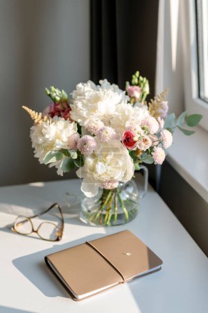 Foto de Un ramo de flores y un cuaderno sobre la mesa a la luz del atardecer. - Imagen libre de derechos