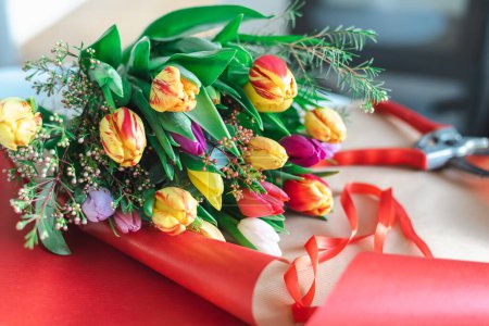 Foto de Un colorido ramo de tulipanes de primavera se encuentra en un papel de envolver rojo brillante. - Imagen libre de derechos