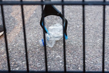 Foto de Un voluntario recogiendo una botella de plástico desechada en una bolsa de basura negra de la hierba. - Imagen libre de derechos