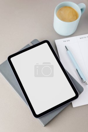 Top view of a digital tablet with a white screen, a pen, a notepad and a cup of fresh coffee. Do it.