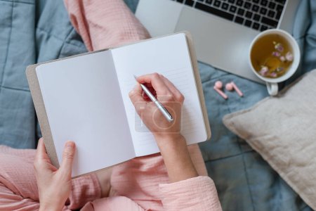 Foto de Una escena en colores pastel de una mujer tomando notas y tomando té caliente en su cama. - Imagen libre de derechos
