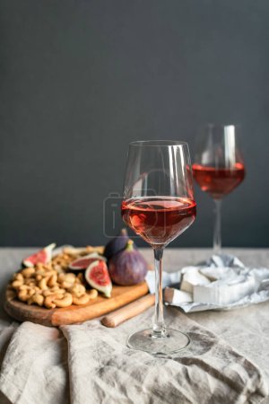 Photo for Rose wine with ripe figs, camembert cheese and cashews on a table indoors. - Royalty Free Image