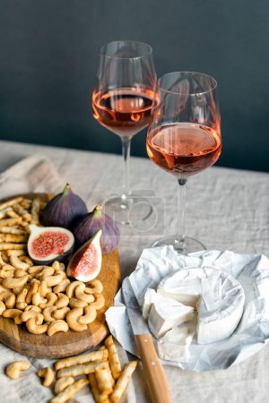 Foto de Vino de rosas con higos maduros, queso camembert y anacardos en una mesa en el interior. - Imagen libre de derechos