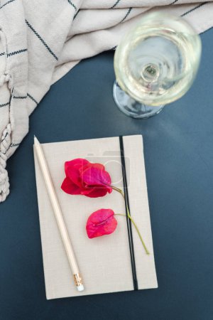 Photo for A notebook with a bougainvillea flower, a pencil, and a glass of wine on the table. - Royalty Free Image