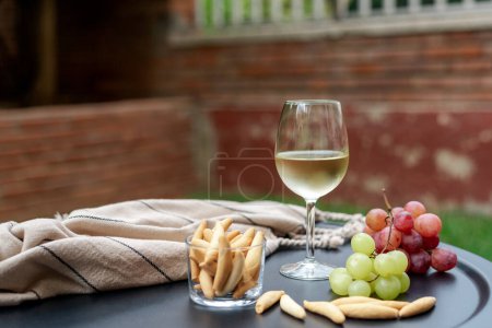 Photo for A glass of white wine with appetizers on the garden table. - Royalty Free Image