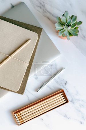 Foto de Escena de escritorio de cuadernos, laptop, bolígrafo, lápiz y suculenta sobre fondo de mármol. - Imagen libre de derechos