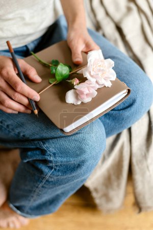 Photo for Woman holds a notepad and a pink rose. - Royalty Free Image