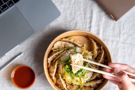 Téléchargez les photos : Boîte à aliments à emporter asiatique avec riz et boulettes sur le bureau près de l'ordinateur portable. - en image libre de droit