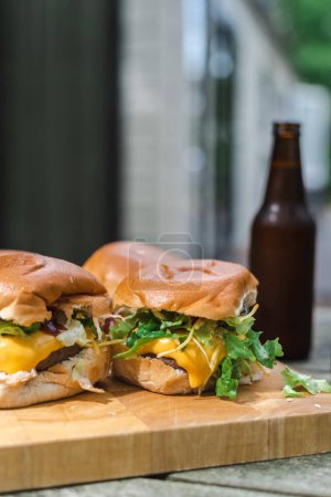 Photo for A set of cheeseburgers on a wooden plate and a couple of beers on an outdoor table. Suburban. - Royalty Free Image