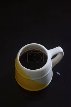 Closeup photo of Black coffee in white and yellow cup on black ceramic table, black background