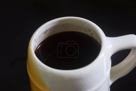 Nahaufnahme Foto von Schwarzer Kaffee in weißer und gelber Tasse auf schwarzem Keramik-Tisch, schwarzer Hintergrund
