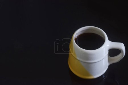 Side view photo of Black coffee in a white and yellow cup on a black ceramic table, black background