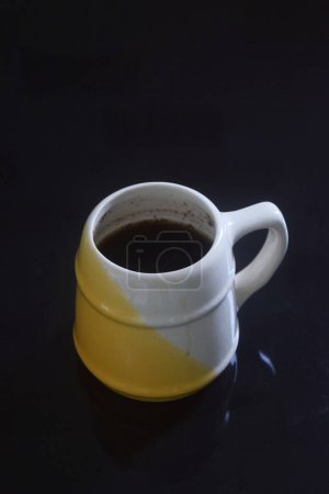 Schwarzer Kaffee in einer weiß-gelben Tasse auf einem schwarzen Keramiktisch, schwarzer Hintergrund