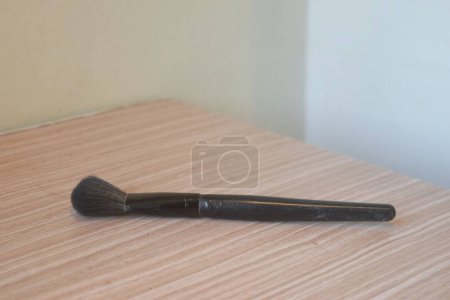 Un pinceau noir utilisé pour appliquer le maquillage est sur une table en bois