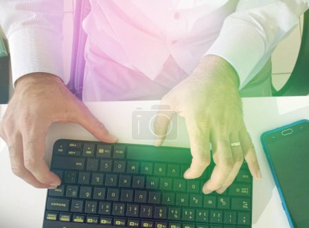 Foto de El hombre de negocios trabaja en la computadora. Solo una imagen de las manos y el teclado. Bajo efecto de luz verde y amarilla. - Imagen libre de derechos