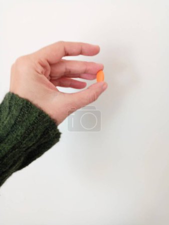 Die Frau hält die Pille zwischen ihren beiden Fingern. Orangefarbene Pille.
