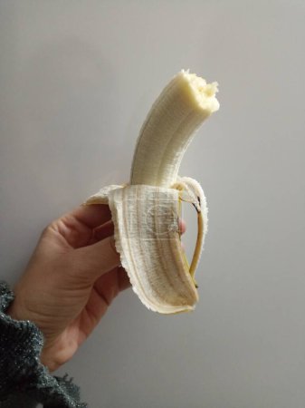 Téléchargez les photos : La femme tient la banane avec sa main. Banane pelée. Une nourriture saine. Banane mordue. - en image libre de droit