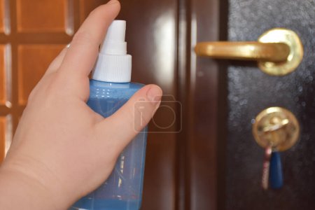 Photo for Woman hand is applying sanitizer on the door handle. Cleaning door handle with alcohol spray for Covid-19. Desinfecting the door handle by spraying alcohol - Royalty Free Image