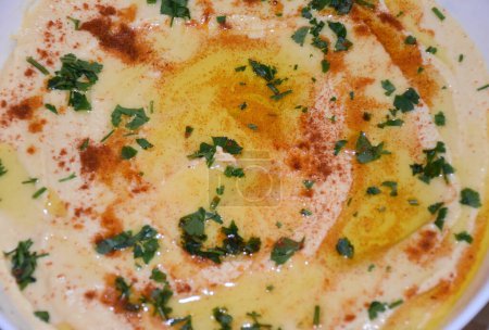 Téléchargez les photos : Hummus texture fond. Assiette de houmous très proche avec de l'huile d'olive, du paprika et du persil saupoudré sur le dessus. Photo de haute qualité - en image libre de droit