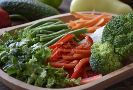 Téléchargez les photos : Mélange de légumes frais hachés sur une assiette en bois. Feuilles de chou frisé, haricots verts, poivrons, carottes, brocoli. Photo de haute qualité - en image libre de droit