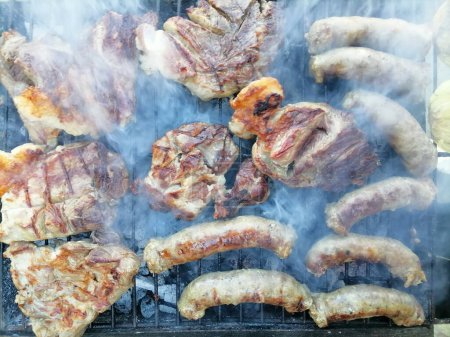 Téléchargez les photos : Steak de porc et saucisses cuites sur le gril, sur le feu de bois. Journée familiale festive avec barbecue. Photo de haute qualité - en image libre de droit