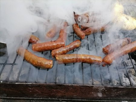 Sausages on a smoking grill, close-up. Sausage BBQ on wood ember, smoking. Barbecue, smoke background. High quality photo