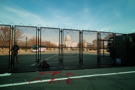 Foto de Un soldado de la Guardia Nacional hace guardia en el edificio del Capitolio de Estados Unidos en Washington, DC. al atardecer, fortificado detrás de una cerca de metal coronada con alambre de afeitar después de la insurrección del 6 de enero de 2021. - Imagen libre de derechos