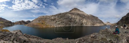 Photo for A panoramic shot of a group of backpackers taking a lunch break next to Long Lake (Lake 10683) in Wyoming's Wind River Range. Mount Victor is seen across the lake. - Royalty Free Image