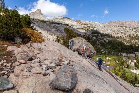Photo for Three male backpackers ascend a steep rock face on the northeast side of Douglas Peak in the Wind River Mountain Range in Wyoming. In the distance, the peak name 'The Fortress' is seen. - Royalty Free Image