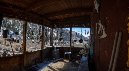 Téléchargez les photos : Une vue depuis le porche de la cabane sur une cabane de mineur abandonnée dans la ville fantôme de Panamint City dans le parc national de Death Valley, Californie. Des carillons éoliens éclectiques sont vus suspendus à la cabine. - en image libre de droit