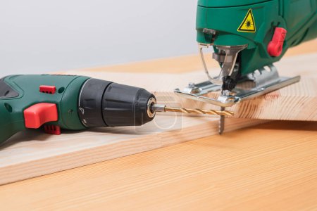 Photo for A man works with a jigsaw and a screwdriver on a wooden table with and without gloves, also measures with a tape measure - Royalty Free Image