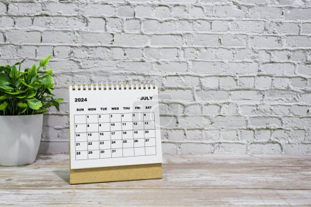 Téléchargez les photos : Calendrier blanc juillet 2024 sur bureau bureau en bois avec plante en pot. Concept du Nouvel An 2024 - en image libre de droit