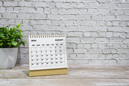 Téléchargez les photos : Calendrier blanc août 2024 sur bureau bureau en bois avec plante en pot. Concept du Nouvel An 2024 - en image libre de droit