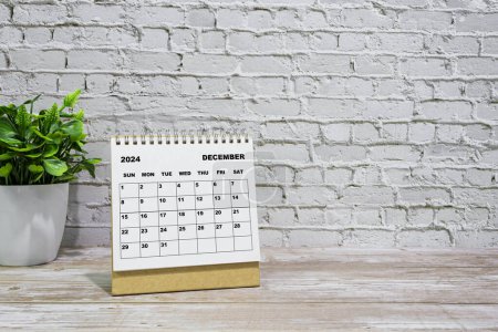 Téléchargez les photos : Blanc Décembre 2024 calendrier sur bureau bureau en bois avec plante en pot. Concept du Nouvel An 2024 - en image libre de droit