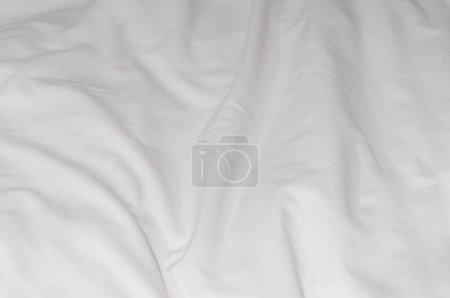 White crumpled or wrinkled bedding sheet or blanket with pattern after guest's use was taken in hotel, resort room with copy space. Untidy blanket background texture