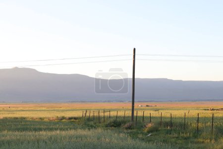 Warm sunset over a tranquil rural landscape with expansive fields and a rural field and distant mountain.