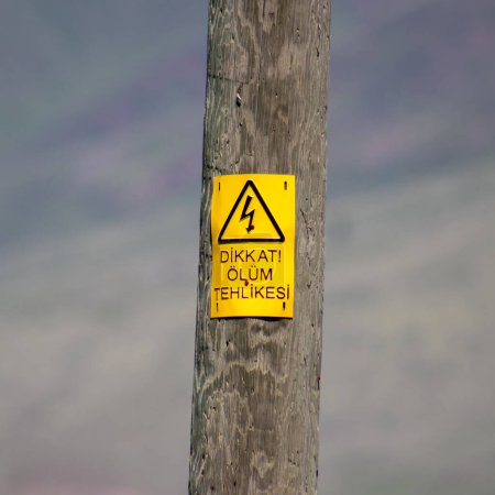 Dikkat Olum Tehlikesi or A weathered wooden utility pole with a yellow warning sign indicating danger of death from electric shock, symbolizing caution. High quality photo