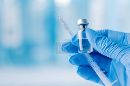 Doctor's hand holding glass vial and syringe with injection over blue background. Vaccination or beauty therapy concept.