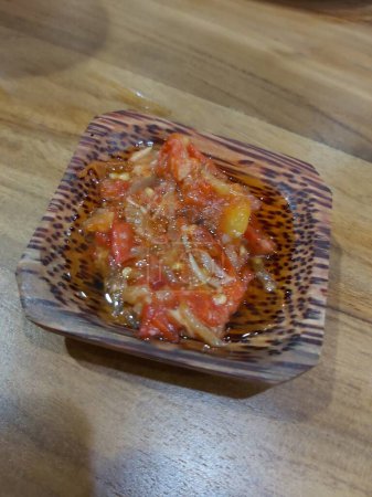 La salsa picante spici de los chiles, las chalotas, el ajo, las especias distintas y los tomates en la escudilla a la mesa de madera. salsa de chile dulce caliente rojo sobre fondo de madera viejo. 
