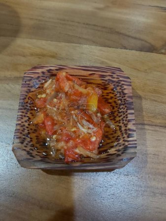 La salsa picante spici de los chiles, las chalotas, el ajo, las especias distintas y los tomates en la escudilla a la mesa de madera. salsa de chile dulce caliente rojo sobre fondo de madera viejo. 