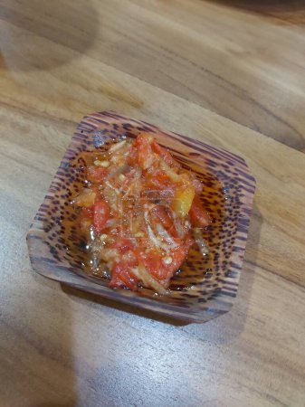 La salsa picante picante de los chiles, las chalotas, el ajo, las especias distintas y los tomates en la escudilla a la mesa de madera. salsa de chile dulce caliente rojo sobre fondo de madera viejo.