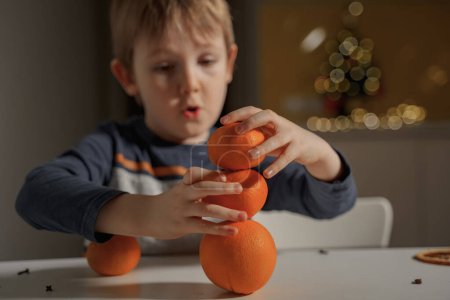 Téléchargez les photos : Le garçon pose trois mandarines comme une pyramide - en image libre de droit