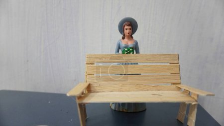 Téléchargez les photos : Selective focus Miniature toy doll women in dress with hat and handicrafts bench chair from ice cream wood - en image libre de droit
