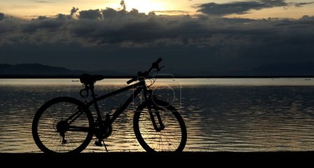 Photo for Silhouette of a bicycle against the background of the sunset on the lake - Royalty Free Image