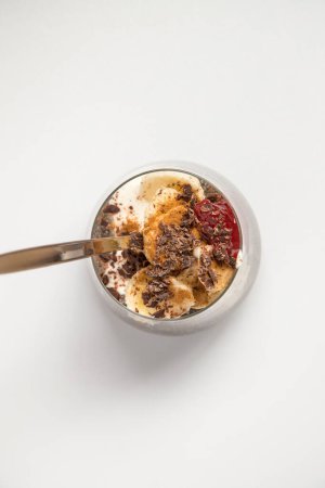 Chia seeds from the Salvia hispanica plant. Glass cup with hydrated seeds, natural yogurt, banana, strawberry jam, cinnamon powder and chocolate shavings. Image seen from above on white background.