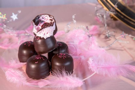 Bonbons à la guimauve éponge recouverts de chocolat et de galette de vanille en dessous, sur un fond rose.
