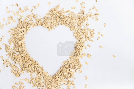 Flocons d'avoine formant une forme de coeur sur fond blanc, image conceptuelle de la bonne nourriture pour la santé. Super aliment riche en nutriments et qui peut être utilisé pour plusieurs recettes. Vue du dessus et espace de copie