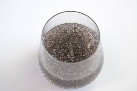 Edible chia seeds from the Salvia hispanica plant. Very healthy functional food to use in various recipes. Glass cup containing the hydrated seeds. Image seen from above on white background.