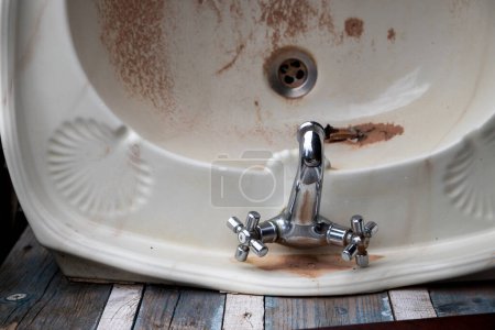 Bild eines Waschbeckens in einem maroden Zustand, ein veraltetes und unbenutztes Objekt auf einem Hintergrund aus altem Holz. Wohnungssanierungskonzept.