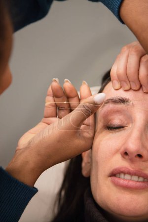 Femme caucasienne enlever les cheveux des sourcils avec la technique du fil fait par le styliste des sourcils. Du fil. Étapes du processus. Gros plan